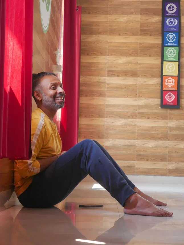 Parveen Nair sitting against a red curtain in the shala, laughing